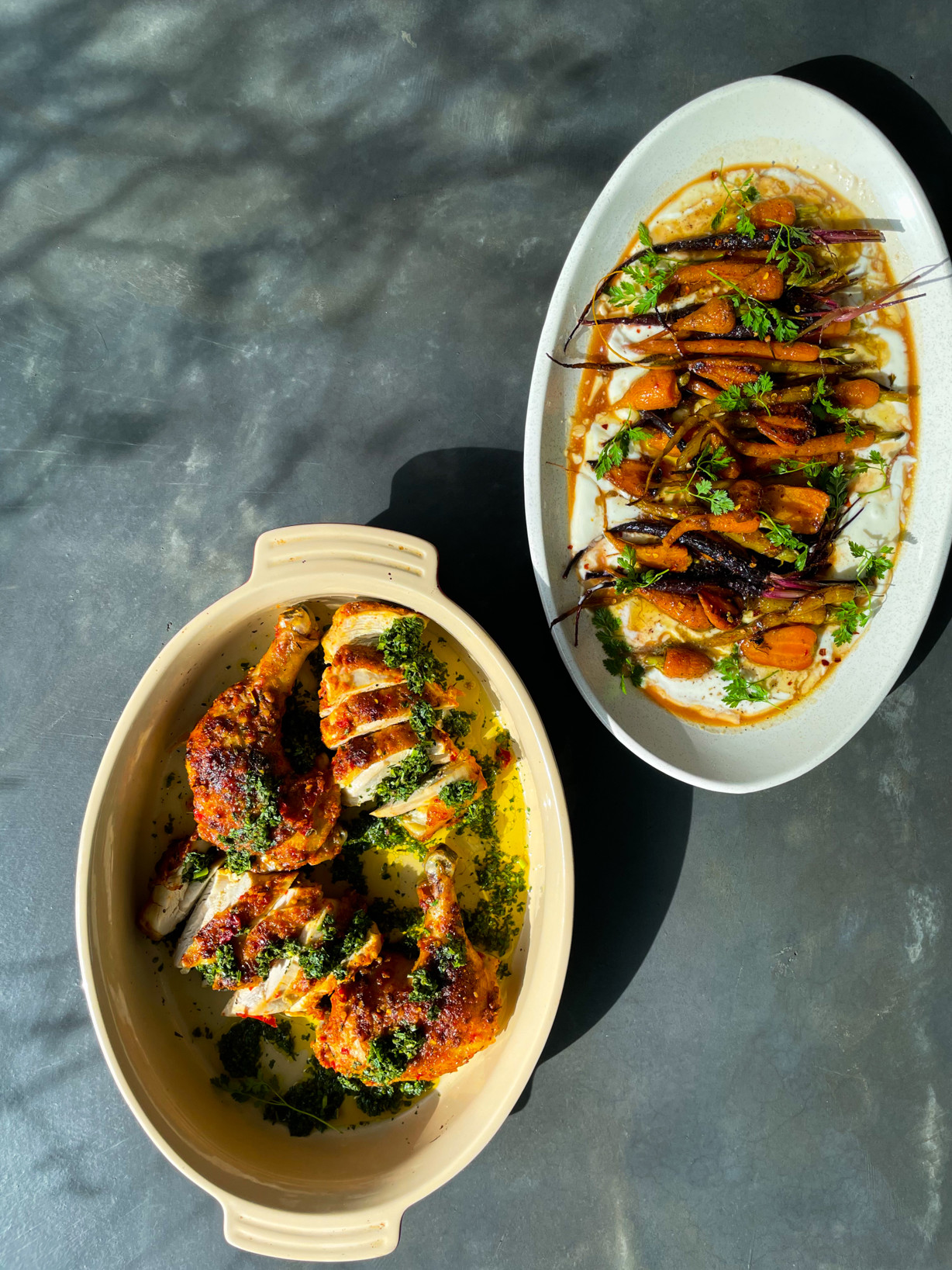 Two dishes bright dishes of roasted chicken and carrots on a dark grey countertop