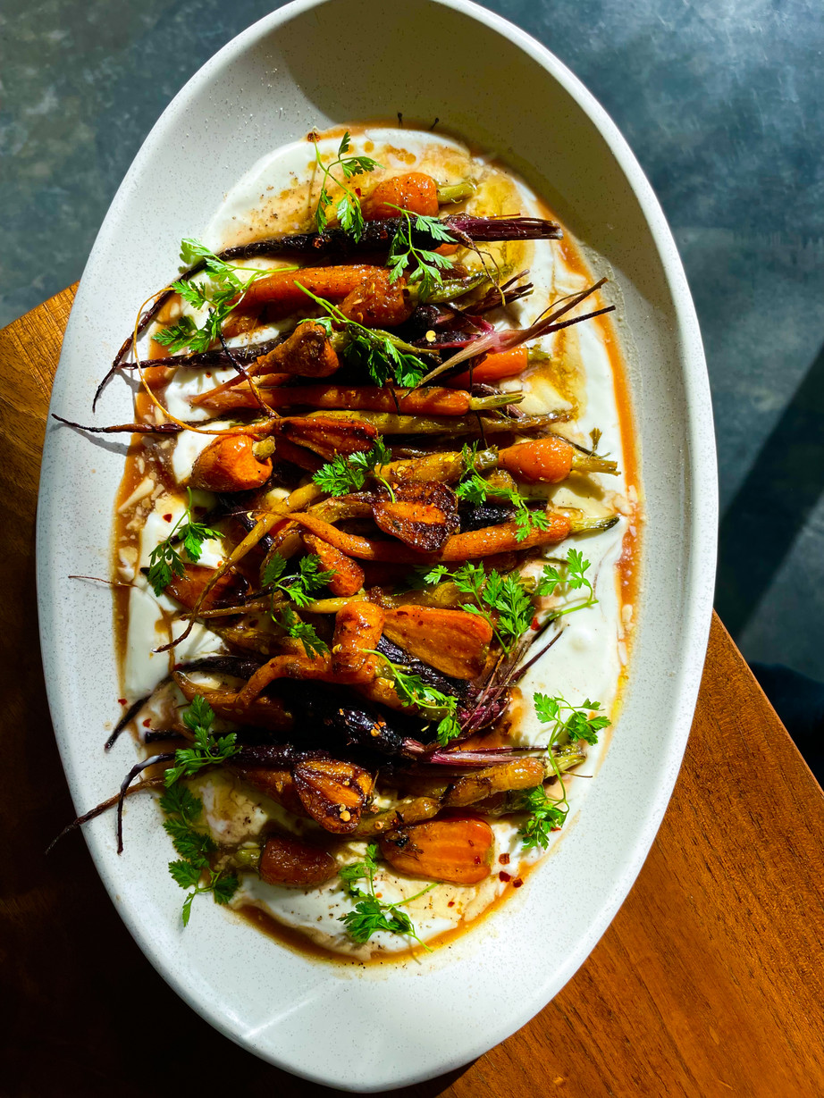 A bright white dish with orange and purple roasted carrots and fresh green parsley